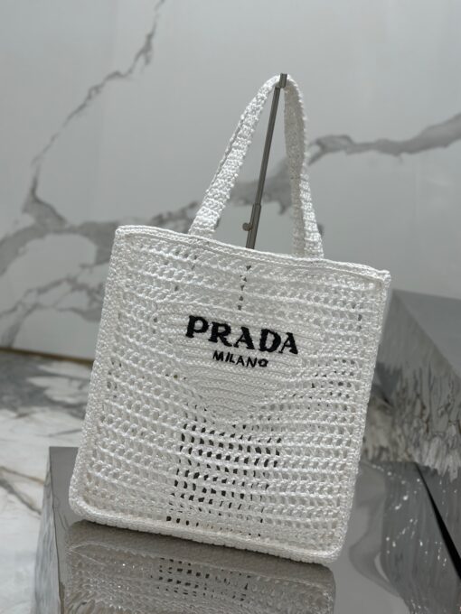 PRADA Crochet Tote Bag. Elevate your style with Prada's signature tote bag. This tote bag is the perfect addition to any summer wardrobe! Adorned with Prada's iconic triangle logo and embroidered lettering, its soft, deconstructed design is made with a light and natural raffia-effect yarn. It's sure to add an elevated touch to your ensemble. | CRIS&COCO Authentic Quality Designer Bags and Luxury Accessories