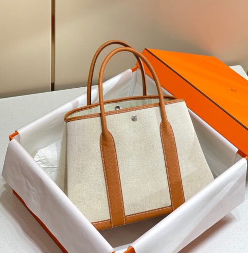 HERMÈS Garden Party: Style for Every Occasion. This Garden Party tote is the perfect blend of style and practicality. This chic and sporty bag is designed for every occasion, whether spending the day amongst the hustle and bustle of the city or enjoying a peaceful weekend in the countryside. Crafted with both leather and canvas, it's the perfect choice for whatever your destination. Not only is it spacious enough to hold your everyday essentials, but it also features Clou de Selle snap closures on the sides for added convenience. This snap that allows the bag to be just the right amount of malleable; to expand and create extra interior space to accommodate larger, or more items at once. Wherever your adventures take you, this exclusive HERMÈS tote will accompany you every step of the way. | CRIS&COCO Authentic Quality Designer Bags and Luxury Accessories