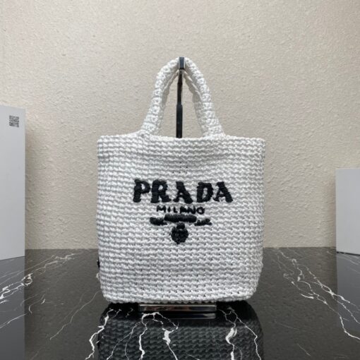 PRADA Small Crochet Tote Bag. Elevate Your Look with an Exquisite Tote Bag! This exquisite tote bag has a deconstructed design made of a light, natural material with a summery mood, raffia-effect yarn. Embroidered lettering logo decorates the front, and the emblematic triangle in enameled metal is the perfect finishing touch to the side. | CRIS&COCO Authentic Quality Designer Bags and Luxury Accessories