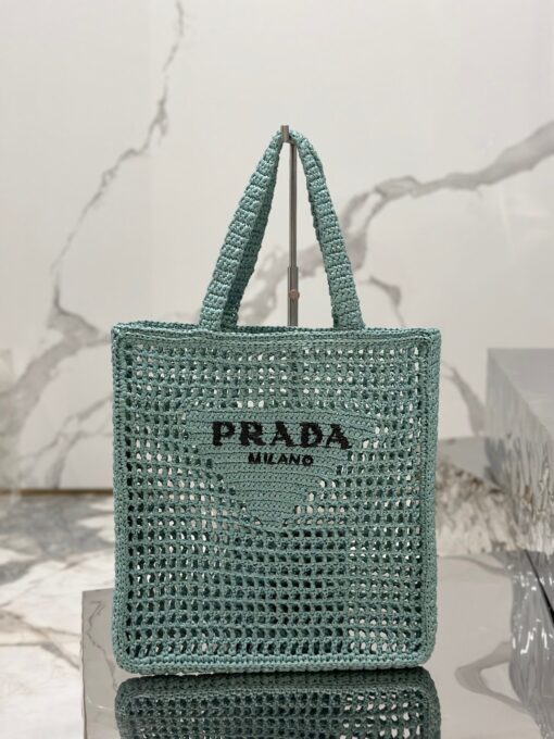 PRADA Crochet Tote Bag. Elevate your style with Prada's signature tote bag. This tote bag is the perfect addition to any summer wardrobe! Adorned with Prada's iconic triangle logo and embroidered lettering, its soft, deconstructed design is made with a light and natural raffia-effect yarn. It's sure to add an elevated touch to your ensemble. | CRIS&COCO Authentic Quality Designer Bags and Luxury Accessories