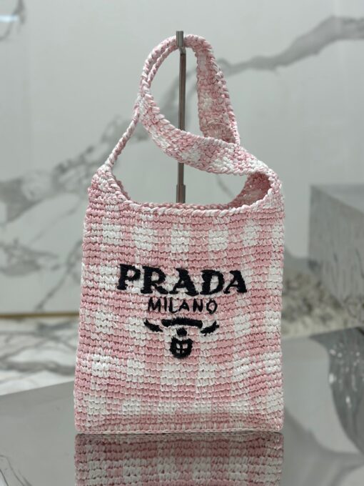 PRADA Crochet Bag- where refined logos meet natural raffia-inspired beauty. Introducing a beautifully crafted tote bag, featuring a gentle, deconstructed design, elegantly crafted from raffia-effect yarn. This lightweight and natural material exudes a delightful summery vibe. The front adorns a sleek enameled metal triangle logo and delicately embroidered lettering logo, engaging in a captivating and harmonious aesthetic conversation.