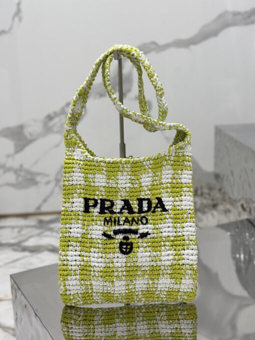 PRADA Crochet Bag- where refined logos meet natural raffia-inspired beauty. Introducing a beautifully crafted tote bag, featuring a gentle, deconstructed design, elegantly crafted from raffia-effect yarn. This lightweight and natural material exudes a delightful summery vibe. The front adorns a sleek enameled metal triangle logo and delicately embroidered lettering logo, engaging in a captivating and harmonious aesthetic conversation.