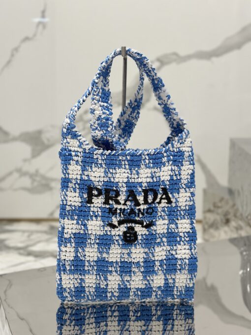 PRADA Crochet Bag- where refined logos meet natural raffia-inspired beauty. Introducing a beautifully crafted tote bag, featuring a gentle, deconstructed design, elegantly crafted from raffia-effect yarn. This lightweight and natural material exudes a delightful summery vibe. The front adorns a sleek enameled metal triangle logo and delicately embroidered lettering logo, engaging in a captivating and harmonious aesthetic conversation.