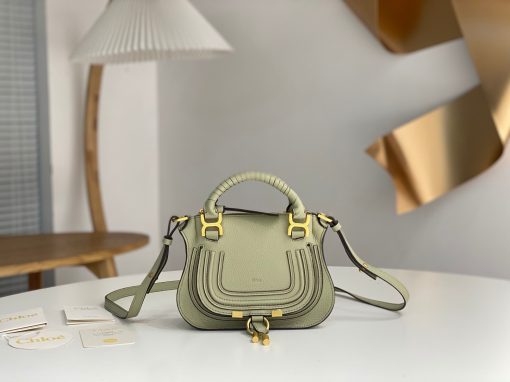 CHLOÉ Marcie Mini Double Carry Bag: Elegance in Miniature. Introducing a charming, petite rendition of the iconic Marcie handbag, this mini double carry bag exudes elegance with its meticulous craftsmanship in grained calfskin. Its clean, sleek lines and gracefully contoured design elevate the relaxed, slouchy silhouette, while the hand-wrapped leather handles impart an artisanal touch. The addition of metallic buckles bestows a polished and refined finish to this exquisite creation. Equipped with both double handles and a long, detachable shoulder strap, this mini bag epitomizes versatility, making it a must-have accessory for any occasion.