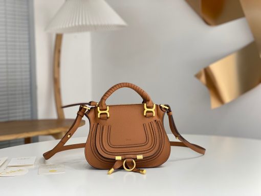 CHLOÉ Marcie Mini Double Carry Bag: Elegance in Miniature. Introducing a charming, petite rendition of the iconic Marcie handbag, this mini double carry bag exudes elegance with its meticulous craftsmanship in grained calfskin. Its clean, sleek lines and gracefully contoured design elevate the relaxed, slouchy silhouette, while the hand-wrapped leather handles impart an artisanal touch. The addition of metallic buckles bestows a polished and refined finish to this exquisite creation. Equipped with both double handles and a long, detachable shoulder strap, this mini bag epitomizes versatility, making it a must-have accessory for any occasion.