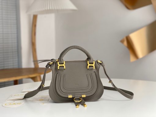 CHLOÉ Marcie Mini Double Carry Bag: Elegance in Miniature. Introducing a charming, petite rendition of the iconic Marcie handbag, this mini double carry bag exudes elegance with its meticulous craftsmanship in grained calfskin. Its clean, sleek lines and gracefully contoured design elevate the relaxed, slouchy silhouette, while the hand-wrapped leather handles impart an artisanal touch. The addition of metallic buckles bestows a polished and refined finish to this exquisite creation. Equipped with both double handles and a long, detachable shoulder strap, this mini bag epitomizes versatility, making it a must-have accessory for any occasion.