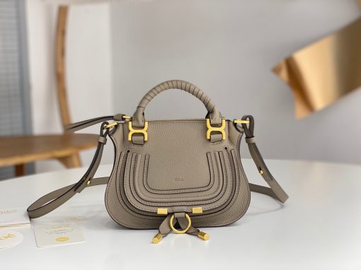 CHLOÉ Marcie Mini Double Carry Bag: Elegance in Miniature. Introducing a charming, petite rendition of the iconic Marcie handbag, this mini double carry bag exudes elegance with its meticulous craftsmanship in grained calfskin. Its clean, sleek lines and gracefully contoured design elevate the relaxed, slouchy silhouette, while the hand-wrapped leather handles impart an artisanal touch. The addition of metallic buckles bestows a polished and refined finish to this exquisite creation. Equipped with both double handles and a long, detachable shoulder strap, this mini bag epitomizes versatility, making it a must-have accessory for any occasion.