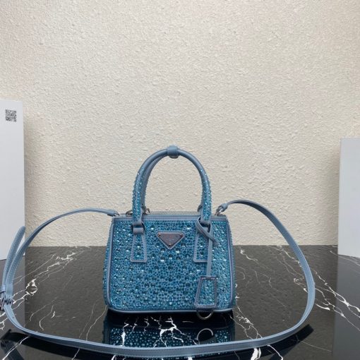 PRADA Galleria Satin Mini Bag With Crystals. Original Quality Bag including gift box, care book, dust bag, authenticity card. A surface of dazzling crystals in various sizes creates a precious play of sparkles and glimmers on this Prada Galleria bag, recalling the jewelry world. The accessory, which exemplifies the centennial excellence of Prada in luxury leather goods, becomes a reflection of the brand's modernity and stylistic identity that seeks to interpret kaleidoscopic contemporaneity through a pragmatic design and structured lines. Presented in a mini version, the bag is made of fine silk satin. The Prada Galleria bag, named after the historic Prada store opened by Mario Prada in 1913 in Galleria Vittorio Emanuele II in Milan, expresses the quintessence of the brand's timeless elegance.