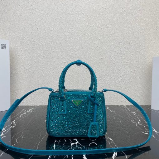 PRADA Galleria Satin Mini Bag With Crystals. Original Quality Bag including gift box, care book, dust bag, authenticity card. A surface of dazzling crystals in various sizes creates a precious play of sparkles and glimmers on this Prada Galleria bag, recalling the jewelry world. The accessory, which exemplifies the centennial excellence of Prada in luxury leather goods, becomes a reflection of the brand's modernity and stylistic identity that seeks to interpret kaleidoscopic contemporaneity through a pragmatic design and structured lines. Presented in a mini version, the bag is made of fine silk satin. The Prada Galleria bag, named after the historic Prada store opened by Mario Prada in 1913 in Galleria Vittorio Emanuele II in Milan, expresses the quintessence of the brand's timeless elegance.
