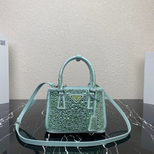 PRADA Galleria Satin Mini Bag With Crystals. Original Quality Bag including gift box, care book, dust bag, authenticity card. A surface of dazzling crystals in various sizes creates a precious play of sparkles and glimmers on this Prada Galleria bag, recalling the jewelry world. The accessory, which exemplifies the centennial excellence of Prada in luxury leather goods, becomes a reflection of the brand's modernity and stylistic identity that seeks to interpret kaleidoscopic contemporaneity through a pragmatic design and structured lines. Presented in a mini version, the bag is made of fine silk satin. The Prada Galleria bag, named after the historic Prada store opened by Mario Prada in 1913 in Galleria Vittorio Emanuele II in Milan, expresses the quintessence of the brand's timeless elegance.