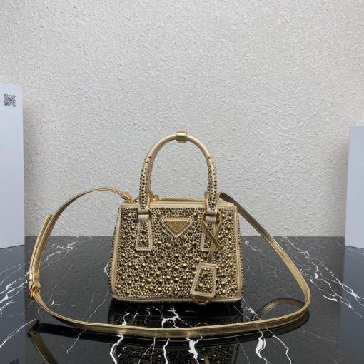 PRADA Galleria Satin Mini Bag With Crystals. Original Quality Bag including gift box, care book, dust bag, authenticity card. A surface of dazzling crystals in various sizes creates a precious play of sparkles and glimmers on this Prada Galleria bag, recalling the jewelry world. The accessory, which exemplifies the centennial excellence of Prada in luxury leather goods, becomes a reflection of the brand's modernity and stylistic identity that seeks to interpret kaleidoscopic contemporaneity through a pragmatic design and structured lines. Presented in a mini version, the bag is made of fine silk satin. The Prada Galleria bag, named after the historic Prada store opened by Mario Prada in 1913 in Galleria Vittorio Emanuele II in Milan, expresses the quintessence of the brand's timeless elegance.