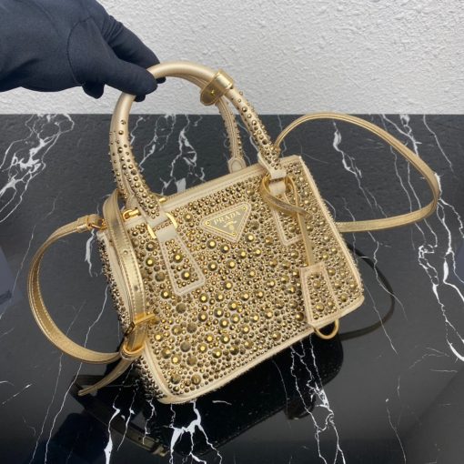 PRADA Galleria Satin Mini Bag With Crystals. Original Quality Bag including gift box, care book, dust bag, authenticity card. A surface of dazzling crystals in various sizes creates a precious play of sparkles and glimmers on this Prada Galleria bag, recalling the jewelry world. The accessory, which exemplifies the centennial excellence of Prada in luxury leather goods, becomes a reflection of the brand's modernity and stylistic identity that seeks to interpret kaleidoscopic contemporaneity through a pragmatic design and structured lines. Presented in a mini version, the bag is made of fine silk satin. The Prada Galleria bag, named after the historic Prada store opened by Mario Prada in 1913 in Galleria Vittorio Emanuele II in Milan, expresses the quintessence of the brand's timeless elegance.