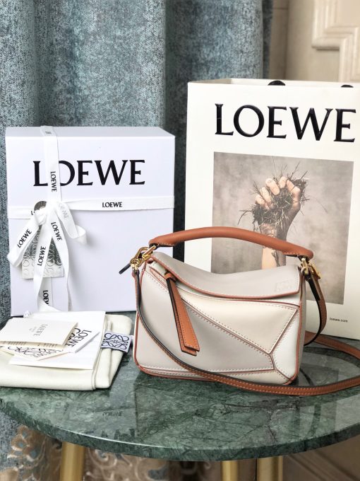 LOEWE Mini Puzzle Bag. Authentic quality luxury bag crafted in genuine leather comes with authenticity card, dust bag and gift bag. Cuboid Shape Meets Precise Craftsmanship The debut bag for *OEWE by Creative Director Jonathan Anderson is the Puzzle bag. With its cuboid shape and precise cutting technique, it boasts distinctive geometric lines. This particular mini version has been expertly crafted using contrasting calfskins.