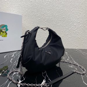 PRADA Re-Edition 2006 Nylon Hobo. Authentic quality luxury bag crafted in genuine leather comes with authenticity card, dust bag and gift bag. Classic Silhouette, Modern Functionality, Unforgettable Style. Crafted from the renowned and recognizable nylon, a fabric emblematic of the brand, this shoulder bag effortlessly melds a timeless design with contemporary and practical elements. Enhancing its appeal are the detachable chain shoulder strap and the Re-Edition leather keyring, further elevating this accessory. - KRIS + KIKO PRADA Re-Edition 2006 Nylon Hobo. Original Quality Bag including gift box, literature, dust bag, authenticity card. Made of iconic nylon, a distinctive fabric of the brand, this shoulder bag combines a classic silhouette and modern, functional details. The accessory is enriched by the detachable chain shoulder strap and the Re-Edition leather keyring.