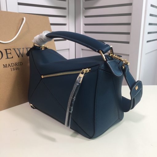 LOEWE 'Puzzle' Shoulder Bag. Authentic quality luxury bag crafted in genuine leather comes with authenticity card, dust bag and gift bag. Unleash the Iconic Cuboid Innovation. The debut bag by Jonathan Anderson has captured the essence of LOEWE and achieved iconic status. This innovative creation showcases a cuboid shape, offering both a remarkable tactile experience and exceptional practicality. The bag's unique volume is achieved through precise cutting, enabling it to be worn in five distinctive styles - from a chic shoulder bag to an elegant clutch - and can even be folded flat for convenient storage. Notable features include the luxurious calfskin craftsmanship, stylish black hand-painted edges, herringbone-patterned cotton-canvas lining, and two internal slip compartments for organized storage. Additionally, a convenient exterior zip back pocket and an embossed anagram add to the bag's functionality and charm. To ensure optimal comfort, the bag also offers a removable adjustable shoulder strap, allowing for a personalized fit.