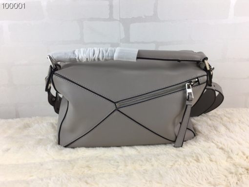 LOEWE 'Puzzle' Shoulder Bag. Authentic quality luxury bag crafted in genuine leather comes with authenticity card, dust bag and gift bag. Unleash the Iconic Cuboid Innovation. The debut bag by Jonathan Anderson has captured the essence of LOEWE and achieved iconic status. This innovative creation showcases a cuboid shape, offering both a remarkable tactile experience and exceptional practicality. The bag's unique volume is achieved through precise cutting, enabling it to be worn in five distinctive styles - from a chic shoulder bag to an elegant clutch - and can even be folded flat for convenient storage. Notable features include the luxurious calfskin craftsmanship, stylish black hand-painted edges, herringbone-patterned cotton-canvas lining, and two internal slip compartments for organized storage. Additionally, a convenient exterior zip back pocket and an embossed anagram add to the bag's functionality and charm. To ensure optimal comfort, the bag also offers a removable adjustable shoulder strap, allowing for a personalized fit.
