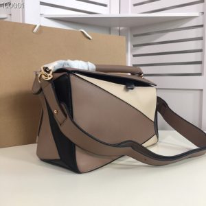 LOEWE 'Puzzle' Shoulder Bag. Authentic quality luxury bag crafted in genuine leather comes with authenticity card, dust bag and gift bag. Unleash the Iconic Cuboid Innovation. The debut bag by Jonathan Anderson has captured the essence of LOEWE and achieved iconic status. This innovative creation showcases a cuboid shape, offering both a remarkable tactile experience and exceptional practicality. The bag's unique volume is achieved through precise cutting, enabling it to be worn in five distinctive styles - from a chic shoulder bag to an elegant clutch - and can even be folded flat for convenient storage. Notable features include the luxurious calfskin craftsmanship, stylish black hand-painted edges, herringbone-patterned cotton-canvas lining, and two internal slip compartments for organized storage. Additionally, a convenient exterior zip back pocket and an embossed anagram add to the bag's functionality and charm. To ensure optimal comfort, the bag also offers a removable adjustable shoulder strap, allowing for a personalized fit. - KRIS + KIKO LOEWE 'Puzzle' Shoulder Bag. Original Quality Bag including gift box, care book, dust bag, authenticity card. The first completely new bag designed by Jonathan Anderson has become a LOEWE icon. With its innovative cuboid shape, extreme tactility and maximum utility, the volume is created through a precise cutting so the Puzzle bag can be worn in five different ways, from shoulder bag to clutch and folds completely until it´s flat. Key features: expertly crafted from calfskin, black hand-painted edges, herringbone-patterned cotton-canvas lining, and two internal slip compartments, handy exterior zip back pocket, embossed anagram. Removable adjustable shoulder strap for the most comfortable length.