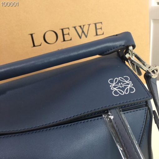 LOEWE 'Puzzle' Shoulder Bag. Authentic quality luxury bag crafted in genuine leather comes with authenticity card, dust bag and gift bag. Unleash the Iconic Cuboid Innovation. The debut bag by Jonathan Anderson has captured the essence of LOEWE and achieved iconic status. This innovative creation showcases a cuboid shape, offering both a remarkable tactile experience and exceptional practicality. The bag's unique volume is achieved through precise cutting, enabling it to be worn in five distinctive styles - from a chic shoulder bag to an elegant clutch - and can even be folded flat for convenient storage. Notable features include the luxurious calfskin craftsmanship, stylish black hand-painted edges, herringbone-patterned cotton-canvas lining, and two internal slip compartments for organized storage. Additionally, a convenient exterior zip back pocket and an embossed anagram add to the bag's functionality and charm. To ensure optimal comfort, the bag also offers a removable adjustable shoulder strap, allowing for a personalized fit.
