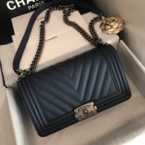 CHANEL Chevron Quilted Leather Flap Bag. Authentic quality luxury bag crafted in genuine leather comes with authenticity card, dust bag and gift bag. A love story in every stitch. The Chanel Boy Flap Bag Quilted is an exquisite creation by the renowned Karl Lagerfeld, paying homage to Gabrielle Chanel's beloved Boy Capel. This iconic design truly represents every woman's ultimate aspiration. Meticulously crafted from high-quality calfskin leather, this bag showcases Chanel's distinctive chevron quilting, complemented by a striking chunky chain link strap adorned with a leather shoulder pad and elegant metal-tone hardware accents. Opening with a captivating CC Boy logo closure, its fabric-lined interior includes a convenient slip pocket, ideal for organizing daily essentials. With its undeniable allure, this sought-after accessory is a luxurious must-have. - KRIS + KIKO CHANEL Chevron Quilted Leather Flap Bag. Original high quality bag. Authentic design. Original quality printed dust bag and sales box. Created by Karl Lagerfeld, the iconic design owes its name to Gabrielle Chanel's first love, Boy Capel. This Chanel Boy Flap Bag Quilted is every woman's dream. Crafted from calfskin leather, the bag features Chanel's signature chevron quilting, chunky chain link strap with leather shoulder pad, and metal-tone hardware accents. Its CC Boy logo closure opens to a fabric-lined interior with slip pocket perfect for daily essentials. A sought-after, luxurious accessory.