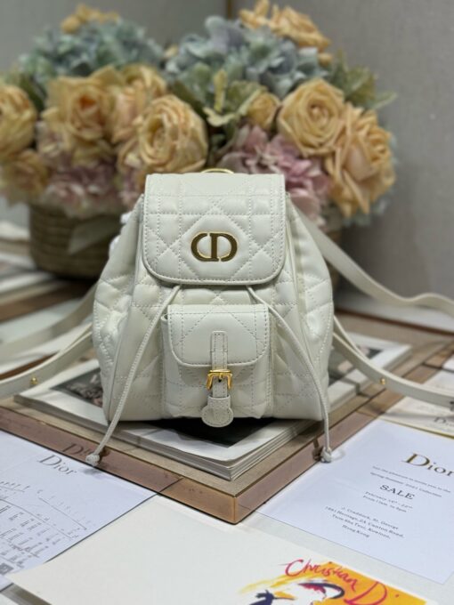 DIOR Small Caro Backpack. Authentic quality luxury bag crafted in genuine leather comes with authenticity card, dust bag and gift bag. Elegance Meets Effortless Edge. Elevate your everyday with the DIOR Small Caro Backpack — a flawless blend of modern femininity and iconic House craftsmanship. Luxuriously crafted in lambskin, its supple silhouette is enhanced by bold Macrocannage topstitching that whispers timeless Dior style. The antique gold-finish ‘CD’ clasp opens to a drawstring main compartment, perfectly balancing beauty and practicality. A discreet flap pocket keeps your daily essentials close at hand, while the top handle and adjustable leather straps offer versatile, all-day comfort. Whether slung over your shoulder or carried by hand, this petite powerhouse delivers Parisian polish in every step.