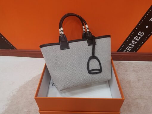 HERMÈS Steeple 25 Bag. Authentic quality luxury bag crafted in genuine leather comes with authenticity card, dust bag and gift bag. Where art meets heritage. The Hermès Steeple Bag is a charming fusion of heritage and artistry, crafted from a blend of canvas and Swift leather. Its design pays tribute to Hermès’ equestrian roots with whip-shaped handles and a stirrup-inspired charm, adding a playful yet sophisticated touch. Lightweight yet spacious, the Steeple is ideal for daily use. Whether you opt for a vibrant motif or a sleek, single-color design, this bag stands out as an artistic expression of luxury that seamlessly integrates into a modern lifestyle. Praised for its unique aesthetic and accessibility within the Hermès lineup, the Steeple Bag is adored by fashion enthusiasts who appreciate its colorful palette and bold personality. While it’s best suited for those who enjoy the texture and look of canvas, it remains a versatile statement piece that captures the spirit of everyday elegance.