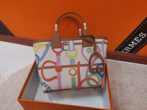 HERMÈS Steeple 25 Bag. Authentic quality luxury bag crafted in genuine leather comes with authenticity card, dust bag and gift bag. Where art meets heritage. The Hermès Steeple Bag is a charming fusion of heritage and artistry, crafted from a blend of canvas and Swift leather. Its design pays tribute to Hermès’ equestrian roots with whip-shaped handles and a stirrup-inspired charm, adding a playful yet sophisticated touch. Lightweight yet spacious, the Steeple is ideal for daily use. Whether you opt for a vibrant motif or a sleek, single-color design, this bag stands out as an artistic expression of luxury that seamlessly integrates into a modern lifestyle. Praised for its unique aesthetic and accessibility within the Hermès lineup, the Steeple Bag is adored by fashion enthusiasts who appreciate its colorful palette and bold personality. While it’s best suited for those who enjoy the texture and look of canvas, it remains a versatile statement piece that captures the spirit of everyday elegance.