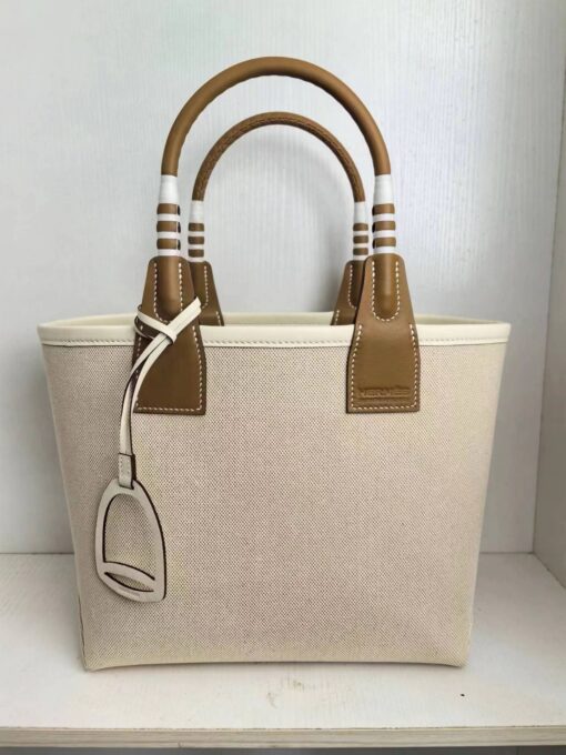 HERMÈS Steeple 25 Bag. Authentic quality luxury bag crafted in genuine leather comes with authenticity card, dust bag and gift bag. Where art meets heritage. The Hermès Steeple Bag is a charming fusion of heritage and artistry, crafted from a blend of canvas and Swift leather. Its design pays tribute to Hermès’ equestrian roots with whip-shaped handles and a stirrup-inspired charm, adding a playful yet sophisticated touch. Lightweight yet spacious, the Steeple is ideal for daily use. Whether you opt for a vibrant motif or a sleek, single-color design, this bag stands out as an artistic expression of luxury that seamlessly integrates into a modern lifestyle. Praised for its unique aesthetic and accessibility within the Hermès lineup, the Steeple Bag is adored by fashion enthusiasts who appreciate its colorful palette and bold personality. While it’s best suited for those who enjoy the texture and look of canvas, it remains a versatile statement piece that captures the spirit of everyday elegance.