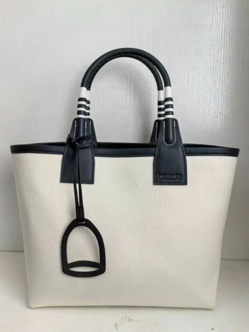 HERMÈS Steeple 25 Bag. Authentic quality luxury bag crafted in genuine leather comes with authenticity card, dust bag and gift bag. Where art meets heritage. The Hermès Steeple Bag is a charming fusion of heritage and artistry, crafted from a blend of canvas and Swift leather. Its design pays tribute to Hermès’ equestrian roots with whip-shaped handles and a stirrup-inspired charm, adding a playful yet sophisticated touch. Lightweight yet spacious, the Steeple is ideal for daily use. Whether you opt for a vibrant motif or a sleek, single-color design, this bag stands out as an artistic expression of luxury that seamlessly integrates into a modern lifestyle. Praised for its unique aesthetic and accessibility within the Hermès lineup, the Steeple Bag is adored by fashion enthusiasts who appreciate its colorful palette and bold personality. While it’s best suited for those who enjoy the texture and look of canvas, it remains a versatile statement piece that captures the spirit of everyday elegance.