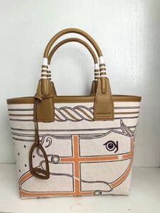 HERMÈS Steeple 25 Bag. Authentic quality luxury bag crafted in genuine leather comes with authenticity card, dust bag and gift bag. Where art meets heritage. The Hermès Steeple Bag is a charming fusion of heritage and artistry, crafted from a blend of canvas and Swift leather. Its design pays tribute to Hermès’ equestrian roots with whip-shaped handles and a stirrup-inspired charm, adding a playful yet sophisticated touch. Lightweight yet spacious, the Steeple is ideal for daily use. Whether you opt for a vibrant motif or a sleek, single-color design, this bag stands out as an artistic expression of luxury that seamlessly integrates into a modern lifestyle. Praised for its unique aesthetic and accessibility within the Hermès lineup, the Steeple Bag is adored by fashion enthusiasts who appreciate its colorful palette and bold personality. While it’s best suited for those who enjoy the texture and look of canvas, it remains a versatile statement piece that captures the spirit of everyday elegance.