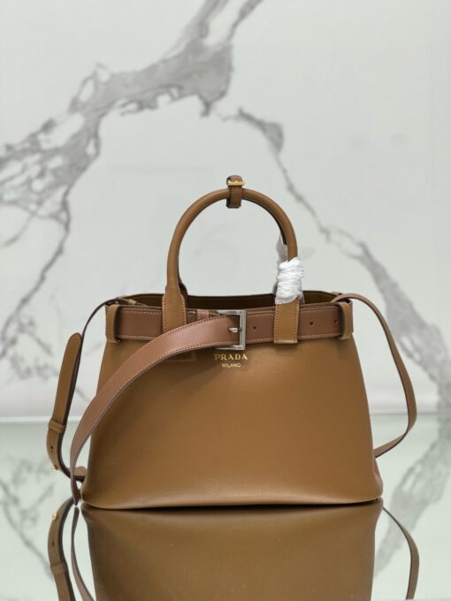 PRADA Buckle Small Leather Handbag. Authentic quality luxury bag crafted in genuine leather comes with authenticity card, dust bag and gift bag. Sophistication Meets Utility. Sleek, structured, and undeniably Prada — the Buckle Small Leather Handbag captures the brand’s signature balance of minimalist elegance and refined detail. Crafted in smooth leather with a buttery-soft nappa interior, this compact piece is a masterclass in functional luxury. A standout feature? Its interchangeable belt strap, adding a bold, modern twist to the timeless silhouette. Whether you're heading to a meeting or a soirée, this bag adapts seamlessly to your mood and moment. Finished with the embossed iconic PRADA logo, it’s a quiet statement of taste and distinction. A versatile companion for the woman who appreciates precision, polish, and just the right touch of edge.