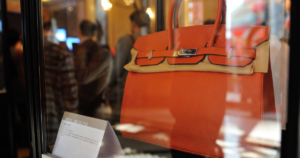 Woman on subway with bright orange replica BIRKIN and oversized sunglasses