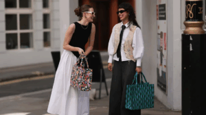 Two women smiling and laughing, wearing black and white outfits, holding colorful patterned bags.